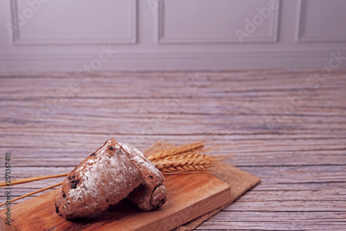 Sliced sourdough sits on wooden board. Sliced to reveal soft, creamy filling inside. Wheat stalks beside it hint at natural ingredients. Rustic wood surface adds warm, inviting tone