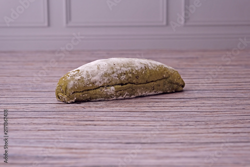 Fresh sourdough dusted lightly with flour rests on wooden surface. Subtle cracks mark its golden crust. Soft lighting enhances texture and warmth. Simplistic background draws focus to baked good