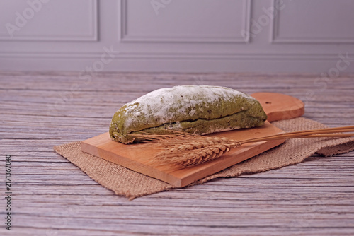 Fresh sourdough dusted with flour rests on wooden board. Golden wheat stalks lie beside it, adding rustic charm. Burlap cloth and warm tones create cozy kitchen ambiance. Perfect for food blogs