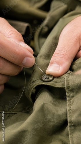 Hand Stitching Button on Olive Garment With Needle and Thread