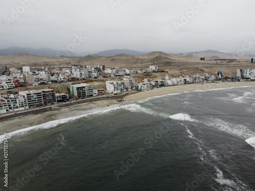 View of Playa Punta Hermosa with coastal buildings, sandy beach, and ocean waves under a cloudy sky in Punta Hermosa, Lima Province, Peru.