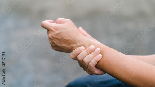 Side view of a person clutching a painful wrist and experiencing hand numbness. Demonstrating peripheral neuropathy, nerve compression, chronic gout, physical exhaustion, and unwellness.