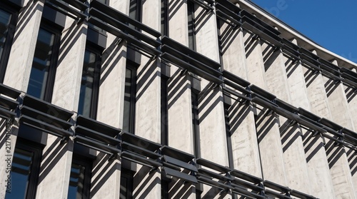 Modern architectural building facade with exposed concrete, horizontal louvers sunshades, vertical windows, and clear blue sky