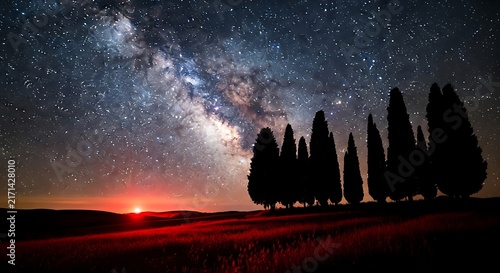 Milky way galaxy shining over cypress trees with a red horizon