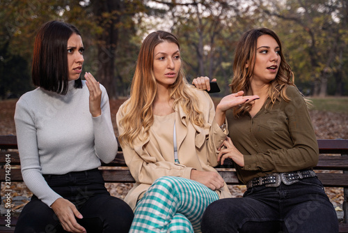 Three young girls on park bench gossiping or shocked by the situation 