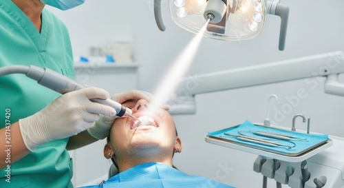 Dentist performing dental cleaning and examination on a patient with modern equipment and bright dental lamp.