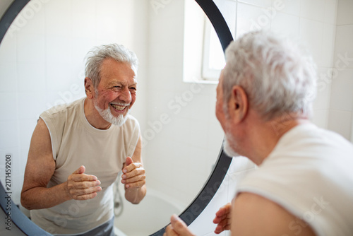 Smiling senior man looking in bathroom mirror at home