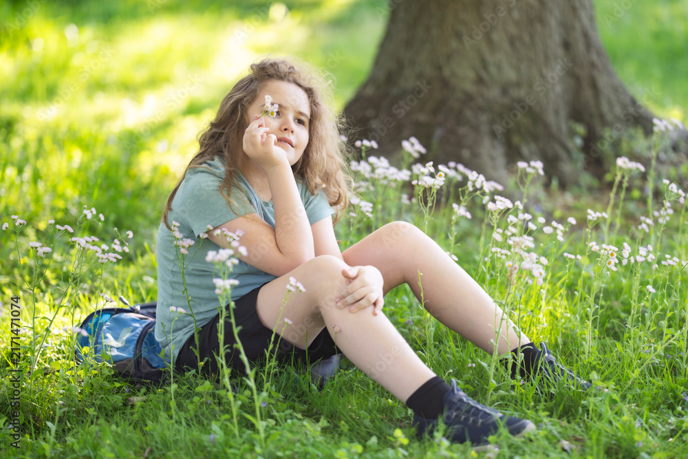 Naklejka premium Meadow flowers frame young girl. Green meadow creates dreamy bokeh. Meadow portrait shows childhood innocence. Meadow scene feels sunny and peaceful.