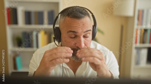 Man wearing headset presses his temples and leans toward a computer monitor in an office building; stress fatigue.