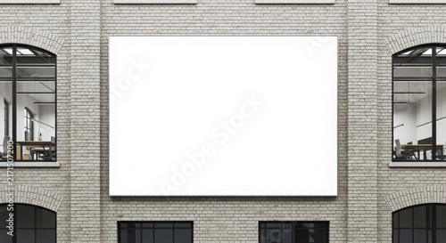 A blank white billboard mounted on a grey brick building facade with large arched windows on either side, showing office interiors.