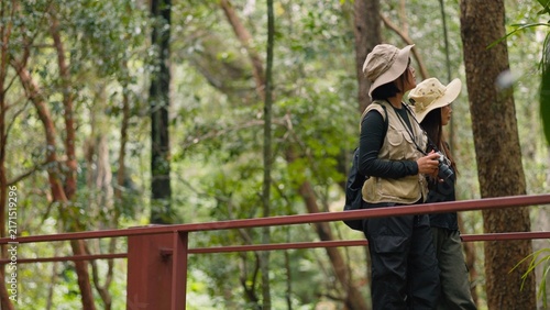 Canvas Print Asian female hikers standing on wooden bridge walkway and enjoying scenic green forest