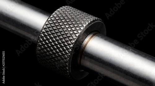 Macro detail of a stainless steel barbell shaft with knurled grip pattern isolated on a black background for gym fitness concept