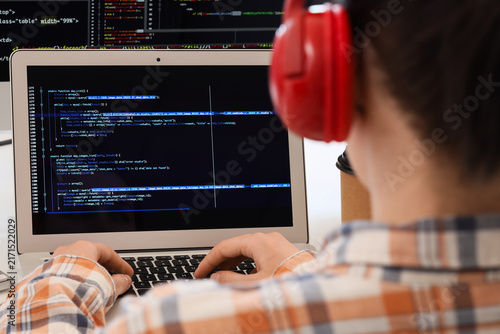 Female programmer with headphones and laptop working at desk in office, closeup