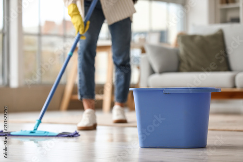 Young woman with plastic bucket mopping floor at home, closeup