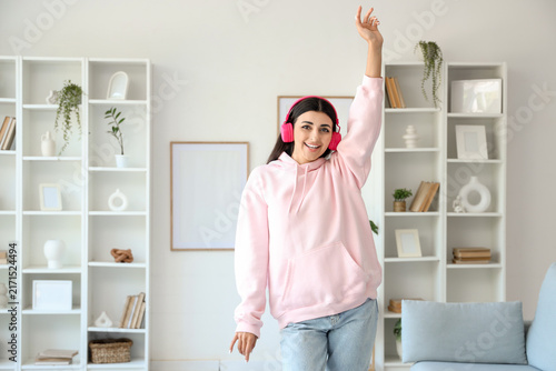 Beautiful young woman in modern headphones listening to music and dancing at ...