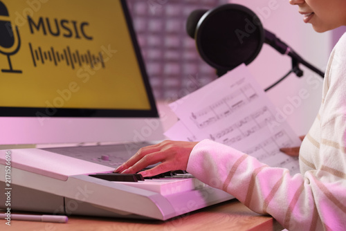Young woman with note sheets playing synthesizer at table in recording studio...