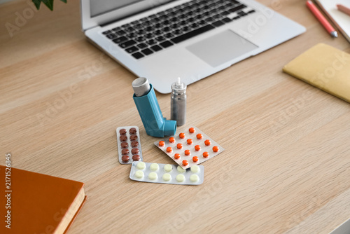 Fotografie Modern inhaler, asthma aerosol canister and pills on workspace desk, closeup