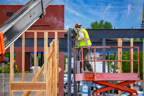 Canvas Print Construction welder on scissor lift working on steel beam frame at building site