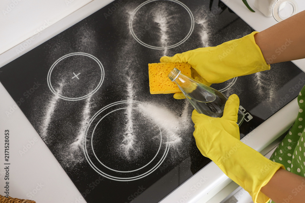 Naklejka premium Housewife cleaning electric stove with vinegar and baking soda in kitchen, closeup