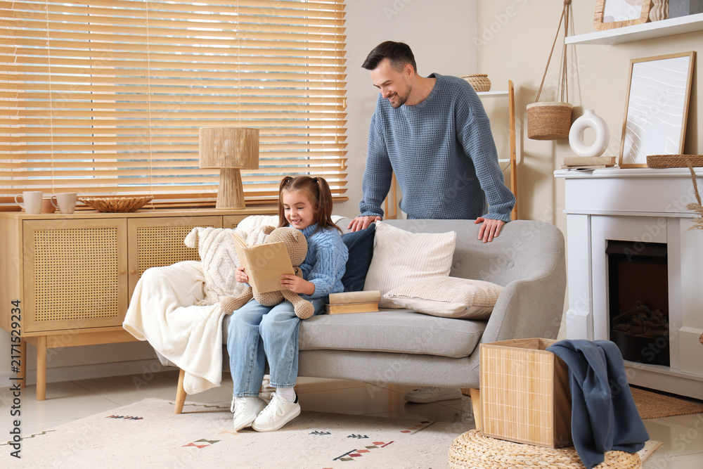 Fototapeta premium Happy father and his daughter in sweaters with teddy bear reading book at home