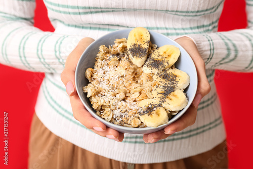 Canvastavla Young woman holding bowl of healthy oatmeal with banana on red background, close