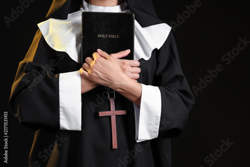 Canvastavla Young nun with Bible on black background, closeup