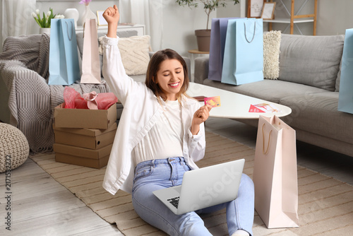 Happy young woman with credit card shopping online at home