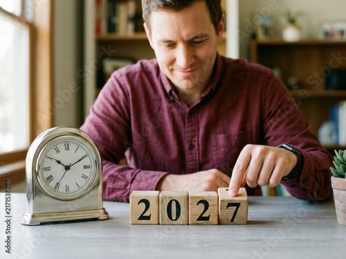 Man placing a wooden block with the number 7 to complete the year 2027 on a desk