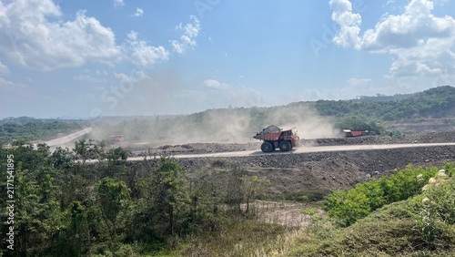 Heavy haul dump truck transporting coal on open pit mining road with dust cloud