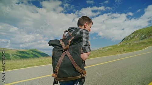 Person walks on a road with a backpack in a mountainous area during daytime