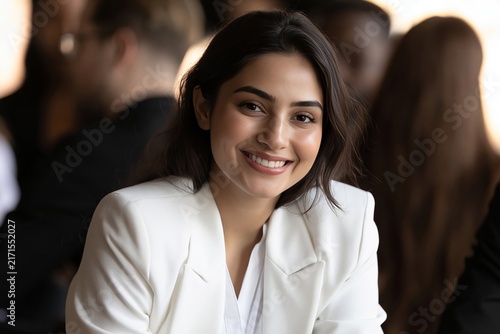 Smiling young businesswoman wearing white blazer looking at camera in office meeting
