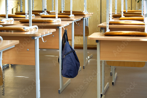 Blue Backpack Hanging on Wooden Desk in Empty School Classroom During Daytime