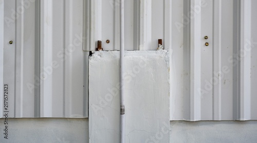 Industrial building facade detail showing corrugated steel siding panels fixed over a white concrete column.
