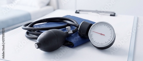 Sphygmomanometer with a white dial on a blue cuff, measuring blood pressure in a medical examination room