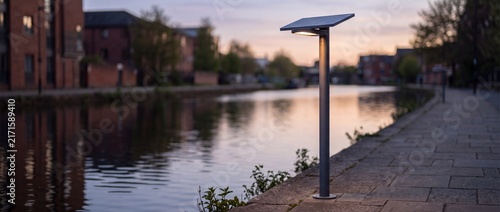 Solar powered street light on sleek metal pole illuminates riverside walkway at dusk using renewable energy for sustainable public safety