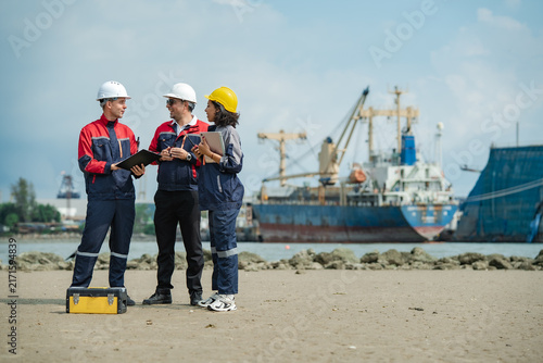 Three marine engineers discussing ship inspection and maintenance plans near cargo vessel, working together at industrial shipyard with copy space.