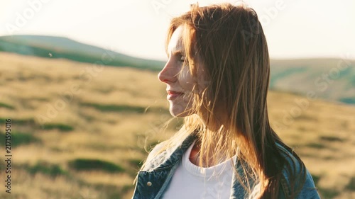 Woman stands in a grassy field during sunset with hills in the background reflecting warm light