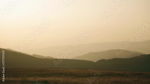 Mountains and hills in the distance during a hazy afternoon with soft light and muted colors near a meadow
