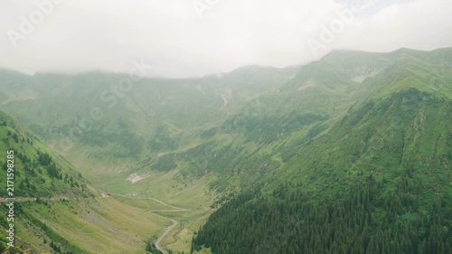 View of a green valley with a winding river, mountains, and cloudy sky in the background during daytime