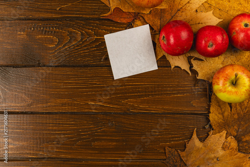 Autumn leaves and apples with a blank card on a wooden table
