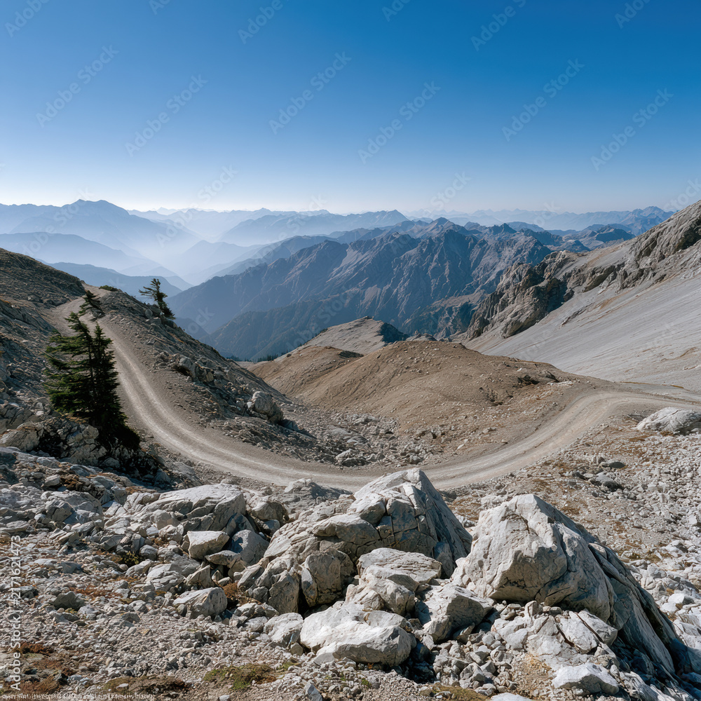 Naklejka premium Mountain range rocky path winding road blue sky rugged terrain panoramic view outdoor adventure nature landscape. winding rocky path cuts through