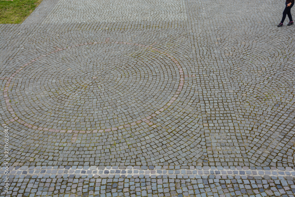 Fototapeta premium Abstract cobblestone pattern with a circular design and partial view of a person walking.