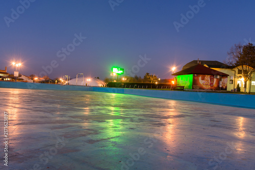 Fotografie Empty ice rink under evening sky with glowing lights reflecting on the surface
