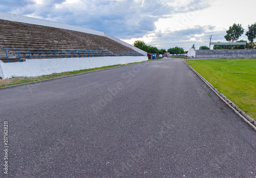 Empty stadium stands and track under a cloudy sky.