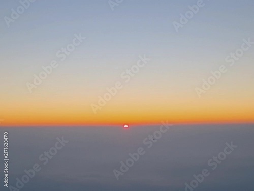 Breathtaking aerial view of a bright red sun rising over a sea of clouds and fog. Peaceful scenic landscape background for nature, environment, and morning concept projects.