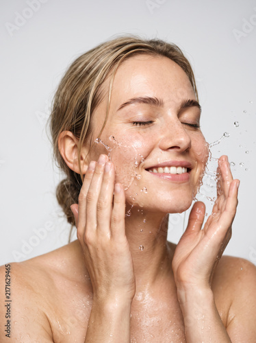 European woman gently splashing water onto her cheeks, a refreshed and happy expression, wet skin with delicate water droplets, skincare commercial aesthetic