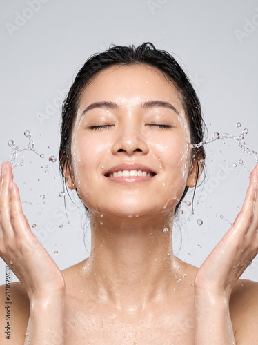premium skincare advertising portrait of a young Asian woman splashing fresh water onto her face,  sophisticated facial cleanser campaign aesthetic, wet glowing skin and detailed water droplets