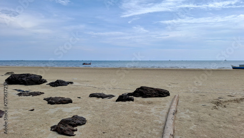 Bild auf Leinwand Minimalist view of small dark rock outcroppings along a vast sandy shore stretching to a calm horizon with small boats in the far distance