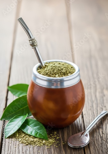 A traditional yerba mate tea set sits on a rustic wooden table, featuring a natural gourd cup with a metal bombilla and loose green leaves, tea, rustic, preparation