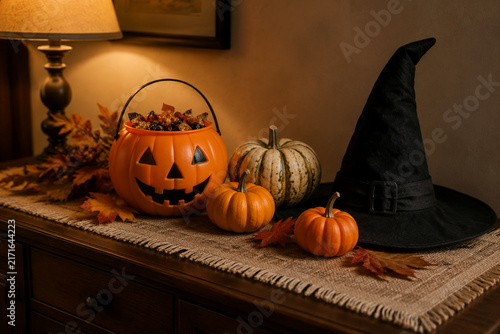 Pumpkin candy bucket with small pumpkins and witch hat on dark oak sideboard, Halloween still life concept